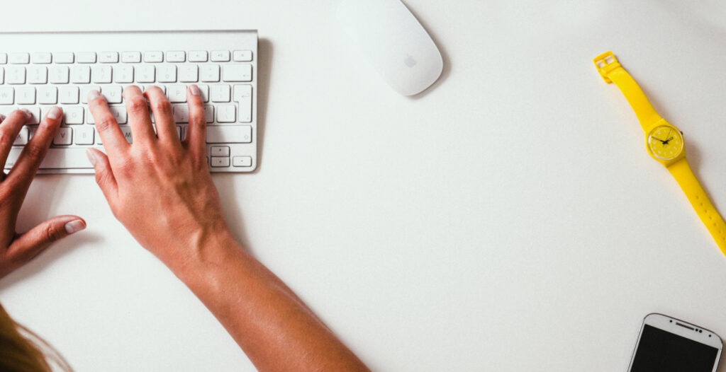 person typing on keyboard next to yellow watch