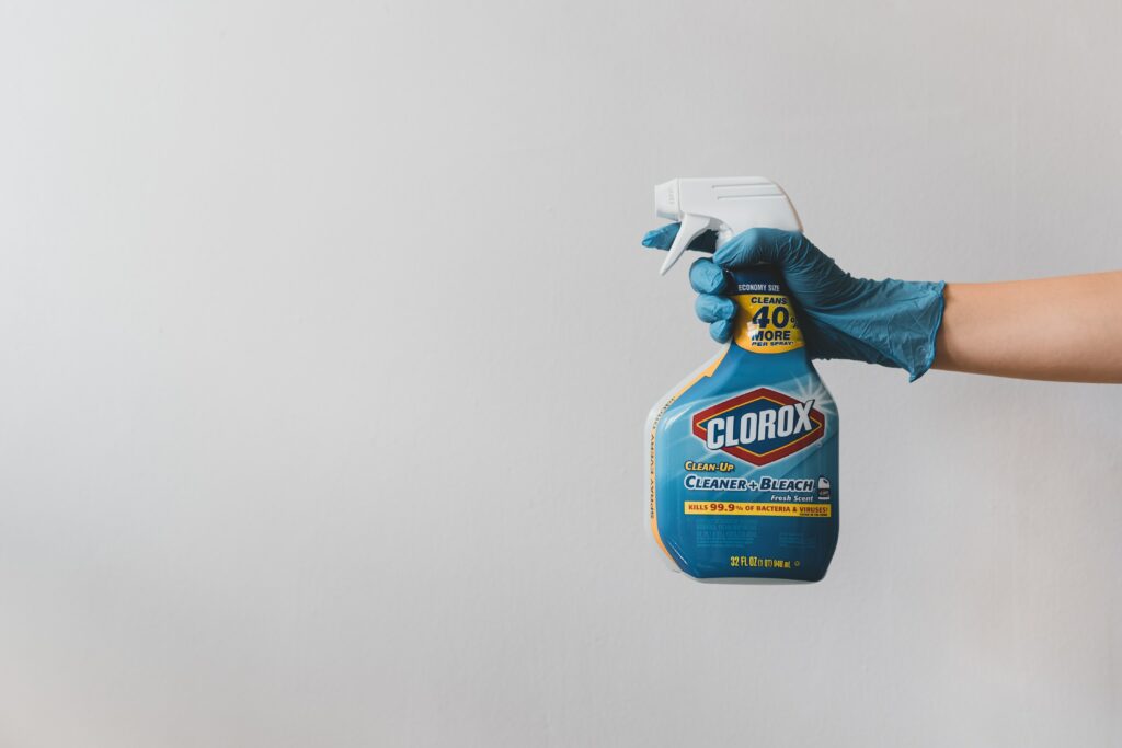 arm with blue rubber glove holding clorox spray bottle for spring cleaning